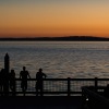 an ocean with people on a dock looking at a boat at sunset