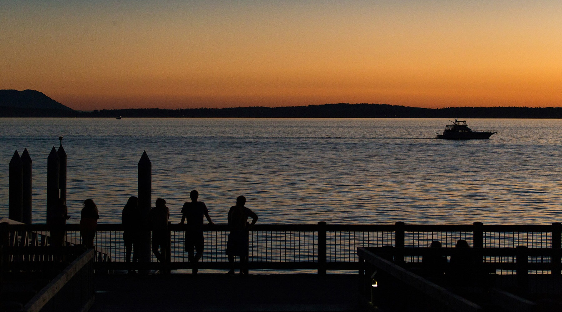 an ocean with people on a dock looking at a boat at sunset